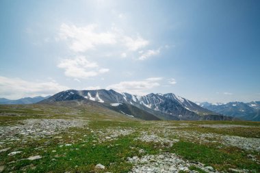 Atmosferik alp manzarası, yeşil çimenleri ve büyük dağ sırtları olan taşlı çayır. Mavi gökyüzünün altında harika karlı dağlar. İskoçya 'da güzel bir yer. Yüksek irtifada görkemli manzara.