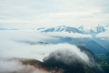 Güzel atmosferik dağlık araziden, buzullu karlı dağ sırtına. Vadideki kayalar arasında dev alçak bulutlar. Harika sakin dağlık arazi manzarası. Bulutların üzerinde uçarak.