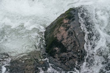 Dağ nehrinin su tabancasındaki kayalarla dolu tam bir çerçeve. Dağ deresinin güçlü su akıntısı. Dağ deresinin hızlı akışının desenli arkaplanı. Islak taşlar yakın plan.