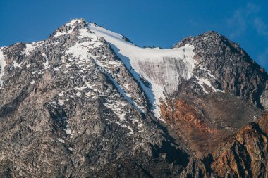 Açık mavi gökyüzünün altında kar olan güzel kahverengi kayaya müthiş bir manzara. Minimum alp manzarası ve buzullu büyük bir dağ. Atmosferik dağ manzarası, güneşli havalarda karlı ve kayalık tepeleri var..