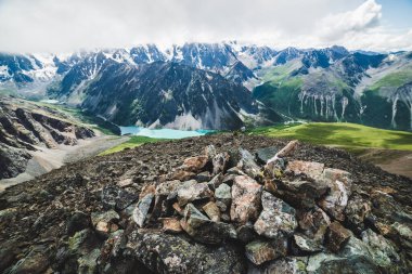 Dağın zirvesinde, manzaralı vadide dev kayalık sıradağlar ve buzullarla çevrili güzel dağ gölü. İnsan yapımı taş yığını ve insanlar üstte. Görkemli vahşi doğa..