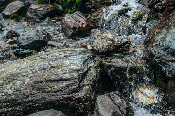 Clear spring water flows on beautiful stony pile slope. Boulder stream with small mountain creek. Wet shiny stones close-up. Nature background with small highland brook. Clear water stream on boulders