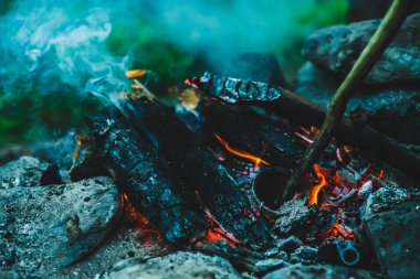 Yanan odun odunları yakın plan ateşte yanmış. Atmosferik sıcak arka plan, turuncu kamp ateşi ve mavi duman. Şenlik ateşinin hayal edilemez tam kare görüntüsü. Güzel ateşte yanan odunlar.