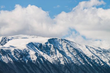Atmosferik dağlık araziden güneşli bir günde karlı dağ sırtına. Dağların zirvesinde gün ışığında kar parlar. Güzel, parlak, karlı bluz. Karla kaplı alçak bulutlar için harika bir manzara.