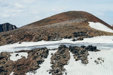 Bulutlu gökyüzünün altındaki Stony Hill 'de buzla kaplı güzel bir buzul. Dağda kar. Kayanın üstünde ateş. Yüksek irtifada atmosferik alp manzarası. Görkemli doğanın harika dağlık arazisi..
