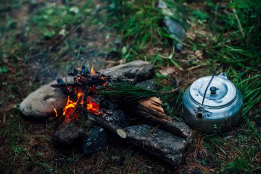 Kamp ısıtıcısı kamp ateşinin yanında. Vahşi doğada rahat bir kamp yeri. Kamp ateşinin harika akşam atmosferik arka planı. Küçük sihirli şenlik ateşinin güzel alevi. Ateşli romantik sıcak bir yer.