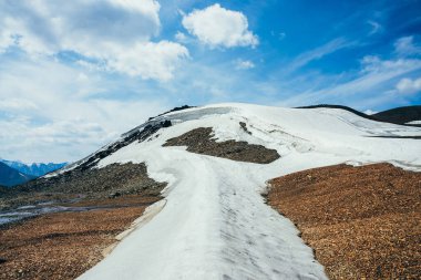 Küçük buzulun üzerinde mavi gökyüzünde bulut taşlı kayaların üzerinde buzla kaplı. Dağda kar, ateş ve eriyen su akıntısı. Yüksek irtifada güzel bir alp manzarası. Muhteşem atmosferik dağ manzarası.