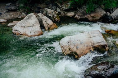 Dağ deresi çağlayanlarıyla birlikte doğanın arka planı. Yeşil suları olan güzel dağ dereleri olan manzaralı bir yer. Küçük bir nehirde yeşil suyu olan cennet manzarası. Hızlı su akışı yakın çekim.