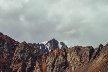 Bulutlu gökyüzünün altında, güzel dağların arkasındaki sivri uçlu kayanın üzerindeki dev buzulun muhteşem manzarası. Atmosferik dağ manzarası, bulutlu bir günde sivri kayalık dağlar.