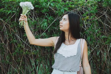 Bahçe bahçesinde yemyeşil karahindiba buketi olan ilham verici bir kız. Baharda yeşil çitin yanında çiçek açan genç bir kız. Kız üzümlerinin arka planında güzel bir kadın portresi.