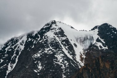 Atmosferik muhteşem manzara, büyük kayalık dağlar ve kötü yağmurlu havada buzullar. Hafif fırtınalı bulutlar karlı dağın tepesine dokunur. Kasvetli gizem bulutlu gökyüzünde karla kaplı bir manzara.