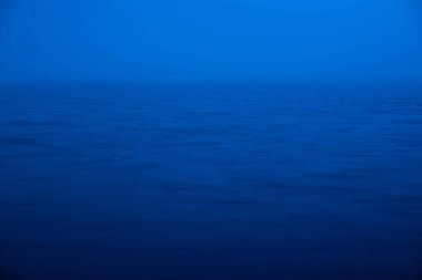 Su dalgalanma doğa arka planı. Mavi klasik renk denizinin doğal dokusu. Alacakaranlıkta derin mavi sakin su. Gölün üzerindeki yoğun sisin meditasyon görüntüsü. Yumuşak ışık su yüzeyinde parlar.
