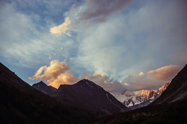 素晴らしい山のシルエットとオレンジの雲と夕日の素晴らしい鮮やかな風景 明け方の空の下で山の偉大なシルエットと大気高地の風景 オレンジの雲に雪の山 — ストック写真