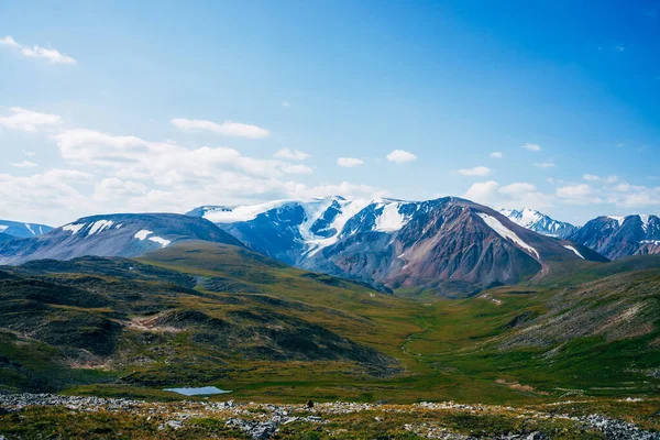Manzaralı küçük alp gölü ve gün ışığında buzullu büyük dağlar. Güneşli bir günde yeşil dağlık vadideki yosunların arasında mavi dağ gölü olan muhteşem yeşil bir manzara. Harika manzara..
