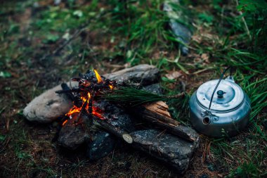 Kamp ısıtıcısı kamp ateşinin yanında. Vahşi doğada rahat bir kamp yeri. Kamp ateşinin harika akşam atmosferik arka planı. Küçük sihirli şenlik ateşinin güzel alevi. Ateşli romantik sıcak bir yer.