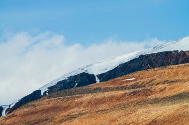 Muhteşem canlı Stony Hill ve güneş ışığında karlı uçurum. Mavi gökyüzünün altında kızıl dağlı, güneşli dağlık bir arazi. Kırmızı turuncu kahverengi tepeli harika bir dağ manzarası..