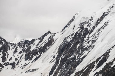 Atmosferik minimalist dağ manzarası. Büyük karlı dağ, büyük bir buzulla birlikte. Büyük kayalık dağların üzerindeki bulutlu gökyüzü. Buzul dili, karla kaplı dağın yamacında. Yüksek irtifada görkemli manzara