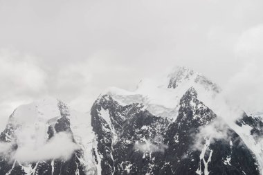 Atmosferik minimalist alp manzarası karlı dağ zirvesinde asılı devasa bir buzulla. Buzul sınırında büyük bir balkon. Karlı dağların arasında alçak bulutlar. Yüksek irtifada görkemli manzara.