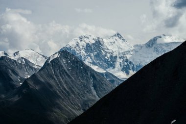 Hava bulutluyken, çok güzel buzul dağları olan muhteşem bir manzara. Bulutlu gökyüzünün altında buzulları olan harika karlı dağ. Kasvetli bulutlu atmosferik manzara Büyük kayalar ve buzullarla.