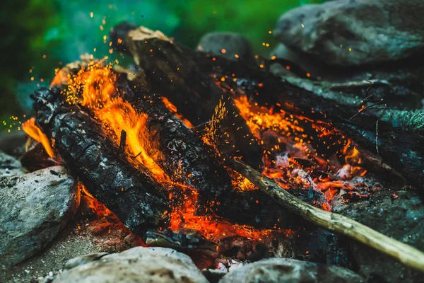 Yanan odun odunları yakın plan ateşte yanmış. Atmosferik arka plan, turuncu kamp ateşi ve mavi duman. Şenlik ateşinin tam kare görüntüsü. Havada parlayan közler. Bokeh 'te parlak kıvılcımlar
