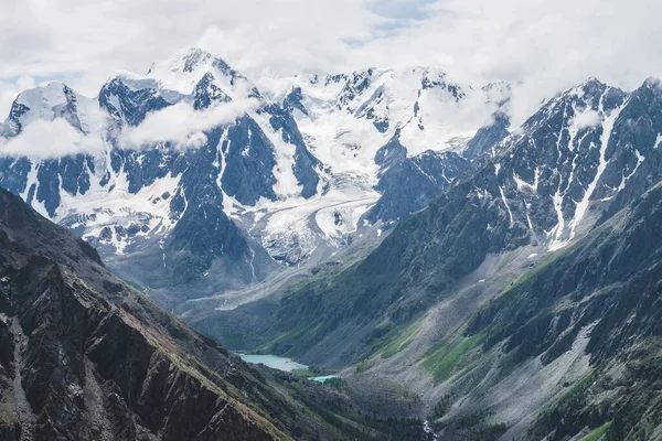 大气高山景观 巨大的冰川悬挂在巨大的岩石和山谷与山地湖泊 大冰川舌 白雪覆盖的高山上的低云 高空壮丽的风景 — 图库照片