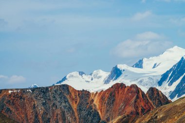 Minimalist, güzel bir dağ manzarası. Kocaman, karlı bir dağ. Sivri uçlu, kırmızı, sarkık bir duvarın arkasında. Mavi gökyüzünün altındaki büyük buzullar. Atmosferik renkli dağ manzaralı dev kırmızı turuncu kahverengi kaya.