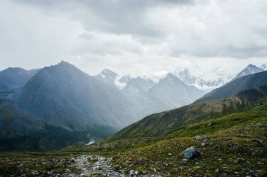 Geçitten büyük dağa atmosferik alp manzarası kasvetli bulutlu gökyüzünün altında keskin bir tepe noktası var. Harika dev sivri kayalık tepeler ve dağ geçidinin arkasındaki karlı dağlar. Dağların muhteşem güzelliği.