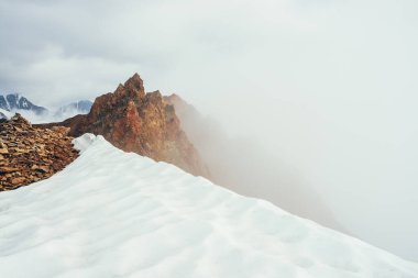 Dağda güzel, sivri kayalık tepeler ve kalın alçak bulutların arasında kar. Atmosferik minimalist alp manzarası. Keskin kayalık dağın tepesi, yoğun bulutların üstünde, uçurumda. Muhteşem dağlık manzara.