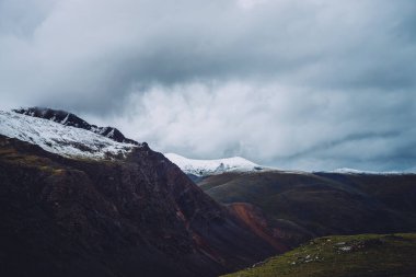 Atmosferik alp manzarası. Büyük karlı dağlar ve gri gökyüzünün altındaki kayalar. Bulutlu havada tepesinde kar olan dev dağlara müthiş bir manzara. Dağlık doğanın dramatik güzellikteki manzarası.