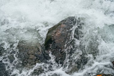 Dağ nehrinin su tabancasındaki kayalarla dolu tam bir çerçeve. Dağ deresinin güçlü su akıntısı. Dağ deresinin hızlı akışının desenli arkaplanı. Büyük taşlar yakın plan.