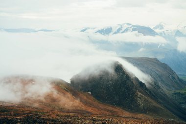 Atmosferik dağlık araziden kayalık dağların tepesindeki dev alçak bulutlara. Highland Vadisi 'nin üzerinde büyük, kalın bulutlar. Yüksek irtifada harika bir manzara. Buzullu, karlı dağ sırasının yamacından manzarayı izle.