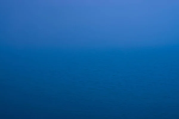 水的脉动是大自然的背景 蓝色经典色彩大海的自然质感 深蓝色平静的海水在黄昏的特写 湖面上方浓雾的映像 水面上柔和的灯光闪烁 — 图库照片