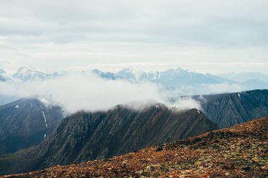 Atmosferik dağ manzarası, büyük kayalıklar ve buzullu dev karlı dağlar. Taş dağdan alçak buluta güzel kayalık tepenin üstünde güzel bir manzara. Harika sakin dağ manzarası..