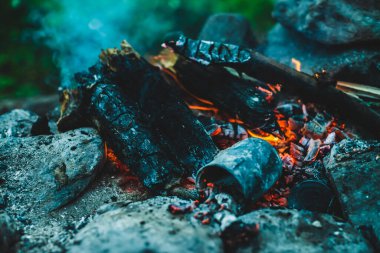 Yanan odun odunları yakın plan ateşte yanmış. Atmosferik sıcak arka plan, turuncu kamp ateşi ve mavi duman. Şenlik ateşinin mükemmel tam kare görüntüsü. Güzel ateşte yanan odunlar.
