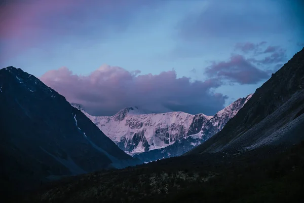 ピンクの雪の山とライラックの雲と夕日の素晴らしい風景 紫の夜明けの空の下で素晴らしい山のシルエットと大気高地の風景 雲の中に紫色の雪のピークへの素晴らしい眺め — ストック写真