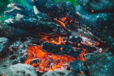 Yanan odun odunları yakın plan ateşte yanmış. Atmosferik arka plan ve turuncu kamp ateşi. Bokeh 'te kıvılcımlar saçan şenlik ateşinin tam kare görüntüsü. Parlayan közlerin sıcak girdabı ve havadaki küller
