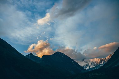 Muhteşem dağ siluetleri ve turuncu bulutlarla gün batımının inanılmaz canlı manzarası. Atmosferik dağ manzarası, şafak vakti gökyüzünün altında büyük dağ siluetleri. Turuncu bulutlarda karlı dağlar
