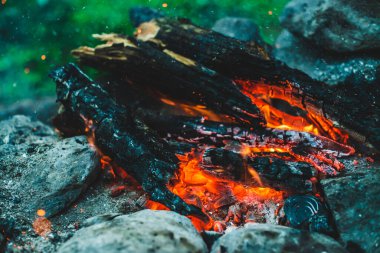 Yanan odun odunları yakın plan ateşte yanmış. Atmosferik arka plan ve turuncu kamp ateşi. Bokeh 'te kıvılcımlar saçan şenlik ateşinin tam kare görüntüsü. Parlayan közlerin sıcak girdabı ve havadaki küller