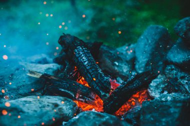 Yanan odun odunları yakın plan ateşte yanmış. Atmosferik arka plan ve turuncu kamp ateşi. Bokeh 'te kıvılcımlar saçan şenlik ateşinin tam kare görüntüsü. Parlayan közlerin sıcak girdabı ve havadaki küller