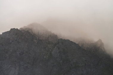 Dev kayalık dağlar arasında dramatik kasvetli sis. Bulutlu gökyüzündeki büyük uçuruma hayali atmosferik bir manzara. Alçak bulutlar ve güzel kayalar. Sisli sabahın erken saatlerinde gizemli bir yerde minimalist bir manzara..