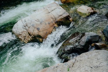 Dağ deresi çağlayanlarıyla birlikte doğanın arka planı. Yeşil suları olan güzel dağ dereleri olan manzaralı bir yer. Küçük bir nehirde yeşil suyu olan cennet manzarası. Hızlı su akışı yakın çekim.