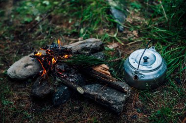 Kamp ısıtıcısı kamp ateşinin yanında. Vahşi doğada rahat bir kamp yeri. Kamp ateşinin harika akşam atmosferik arka planı. Küçük sihirli şenlik ateşinin güzel alevi. Ateşli romantik sıcak bir yer.
