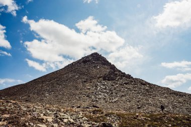 Mavi bulutlu gökyüzünün altında gri kaya zirvesi olan atmosferik dağ manzarası. Güneş ışığında sivri kayalık tepeli harika bir dağ manzarası. Keskin taşları olan güzel kayalık bir dağ tepesi. Noktalı tepe.