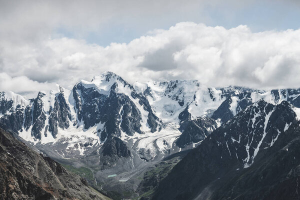 Atmospheric alpine landscape with massive hanging glacier on giant mountain. Big glacier tongue on mountainside. Low clouds among snowbound mountains. Cracks on ice. Majestic scenery on high altitude.