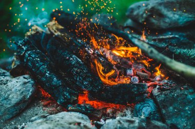 Yanan odun odunları yakın plan ateşte yanmış. Atmosferik arka plan, turuncu kamp ateşi ve mavi duman. Havada parlayan közleri olan şenlik ateşinin tam kare görüntüsü. Parlak kıvılcımlar