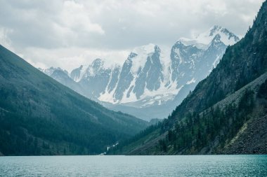 Amazing view to big snowy mountains and mountain lake with azure clear water. Atmospheric scenery with turquoise alpine lake and great mountain with glacier. Giant snowy ridge and shiny water ripples.