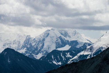 Kötü bulutlu havada devasa buzul dağlarıyla muhteşem bir manzara. Hafif fırtınalı bulutlar karlı dağın tepesine buzullarla dokunur. Dağlar yüzünden fırtına geliyor. Kasvetli bulutlu atmosferik manzara.