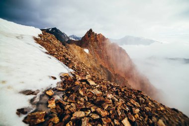 Dağda güzel, sivri kayalık tepeler ve kalın alçak bulutların arasında kar. Atmosferik minimalist alp manzarası. Keskin kayalık dağın tepesi, yoğun bulutların üstünde, uçurumda. Muhteşem dağlık manzara.