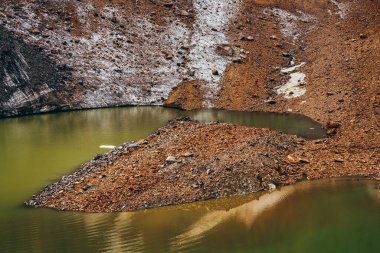 Dağın tepesindeki buzul yamacındaki taşlar asit yeşili renkte. Güzel zümrüt buzul gölü ve taşlı buzulun karlı yamacı. Sıradışı yeşil tonlardan oluşan harika bir alp gölü. İnanılmaz manzara.