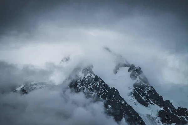 夕暮れ時の低雲の中に雪の山の頂上と神秘的な劇的な高山風景 夕暮れ時の曇り空の氷河へのブレークビュー 濃霧の中で雪の岩と大気ミニマルな風景 — ストック写真